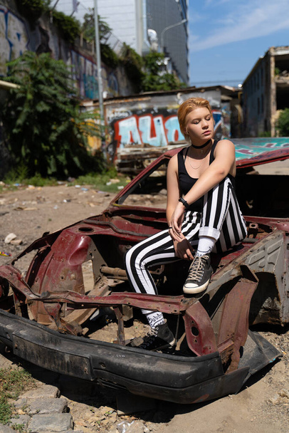 glamorous girl in pants and short hair and makeup posing near a broken old car - Foto, afbeelding