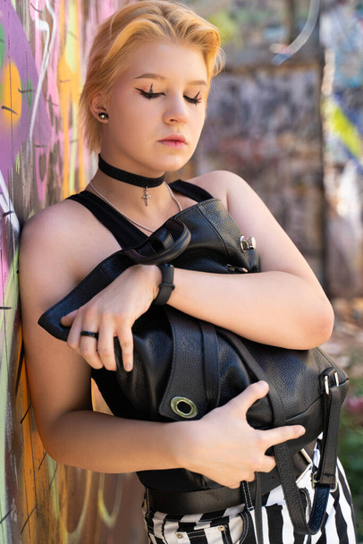 une fille à la mode avec une coiffure courte et lumineuse et des poses de maquillage franches sur le fond d'un mur de graffiti - Photo, image