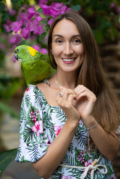 een mooi meisje met een papegaai op haar schouder lacht - Foto, afbeelding