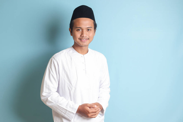 Portrait of Asian muslim man in white koko shirt feeling confident, smiling and looking at camera. Isolated in blue background - Photo, Image