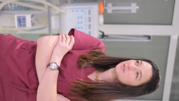 Verticale video van een mooie vrouwelijke arts in speciale kleding in het kantoor van haar kliniek. De dokter kijkt vol vertrouwen naar de camera en glimlacht. 4k video - Video
