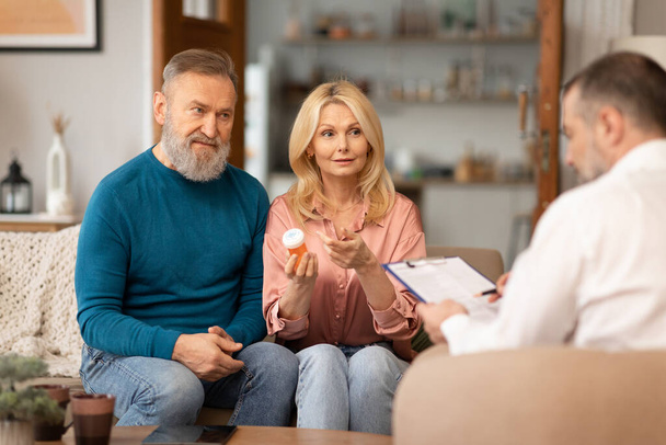 Mature Couple Consulting With Health Advisor Holding Vitamins Pills Sitting Indoor. Spouses Talking With Doctor Or Nutrition Specialist About Medical Supplements And Treatment. Selective Focus - Фото, зображення