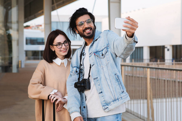 Travel blog. Happy millennial multiethnic male and female tourists take selfie on smartphone, shooting video in city outdoor. Social networks, app for trip, vacation together - Φωτογραφία, εικόνα