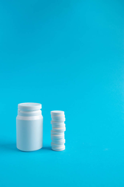 Plastic medical container and white tablets on a blue background viewed from the side. Medical and health concept. 3d rendering. - Фото, зображення