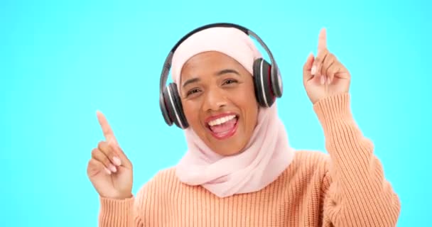 Koptelefoon, dans en vrolijke vrouw geïsoleerd op blauwe achtergrond luisteren naar muziek in viering en winnen. Winnaar, dans en gezicht van moslim persoon in hijab, audio streaming technologie en studio. - Video