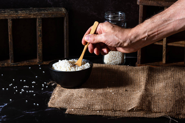 Hand hält einen Kochlöffel, um Reis aus einer Schüssel zu gießen. - Foto, Bild