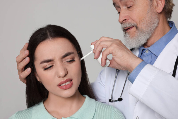Doctor spraying medication into woman's ear on light grey background, closeup - 写真・画像