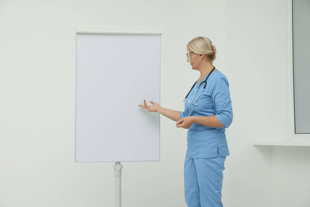 Professional doctor explaining something near flipchart indoors - Foto, Bild