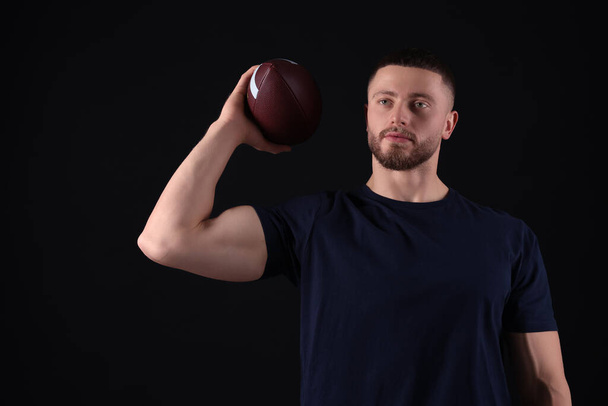 Athletic young man with American football ball on black background - Φωτογραφία, εικόνα