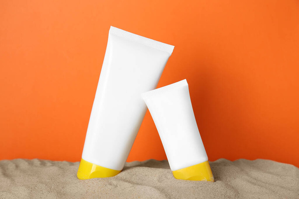 Different suntan products on sand against orange background - Fotografie, Obrázek