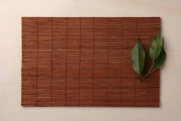 Bamboo mat and green leaves on beige table, top view. Space for text - Foto, afbeelding