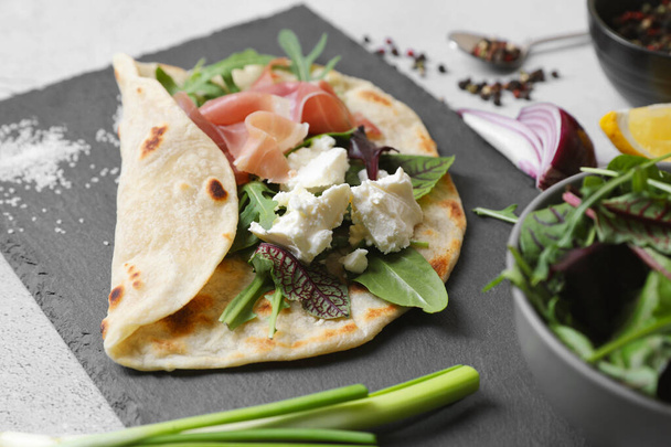 Delicious pita wrap with jamon, cheese cream and greens on light gray table, closeup - Photo, image