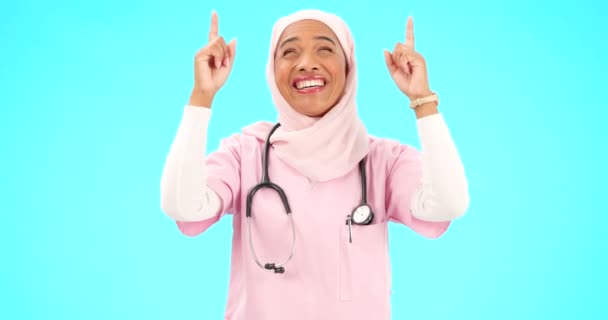 Moslim verpleegster, gelukkige vrouw en wijzend vingerportret met ruimte voor gezondheidszorg, religie of geluk. Islamitische vrouwelijke arts met de hand, glimlach en hijab voor aankondiging op blauwe achtergrond. - Video