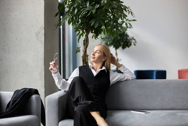 Geschäftsfrau schaut auf Fenster und hält Brille in modernem Büro, macht Pause, entspannt sich - Foto, Bild