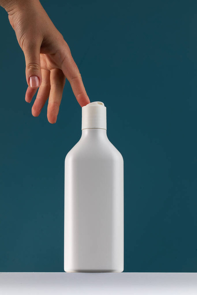 A womans hand reaches for a bottle of cosmetics. White mock-up with shower gel, shampoo with a place for your logo. - Фото, изображение