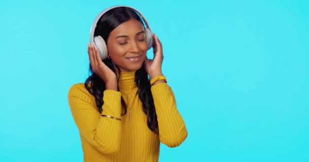 Woman, music and headphones with dance in studio for listening, relax and sound for peace of mind. Gen z girl, streaming audio and happy student with sexy dancing to internet radio by blue background. - Footage, Video