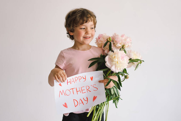 Cheerful happy child with Peonys bouquet. Smiling little boy on white background. Mothers Day concept - Photo, image