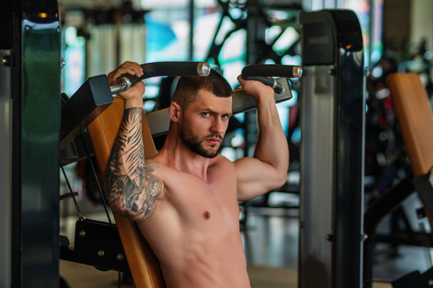 Muscular man workout in the gym. Athletic man having weight training in gym. Handsome man with strong muscles workout in the gym. Portrait of sexy muscular male with dumbbells. Bodybuilder exercise - Photo, Image