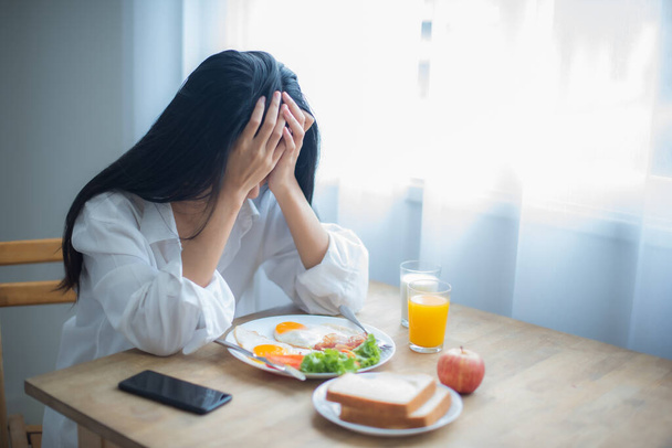 Mooie aziatische vrouw zit zo gestrest dat ze weigert te ontbijten. - Foto, afbeelding