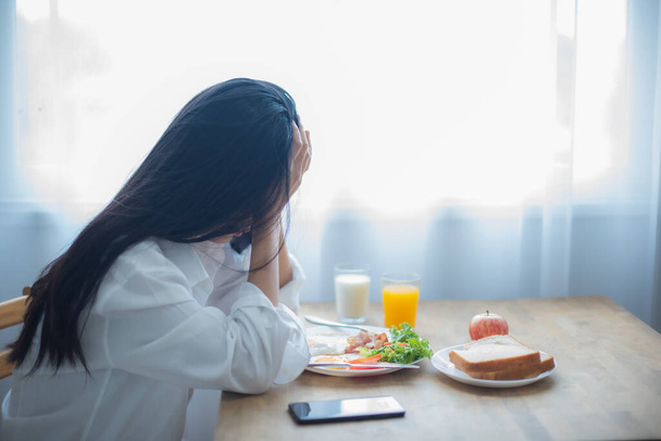 Mooie aziatische vrouw verdriet als ze luisterde naar het slechte nieuws op haar telefoon tijdens het zitten om te ontbijten. - Foto, afbeelding