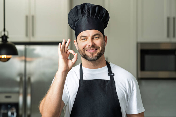 Chef cook with ok sign, delicious food. Handsome man in chefs uniform with chefs hat cooking in the kitchen - 写真・画像