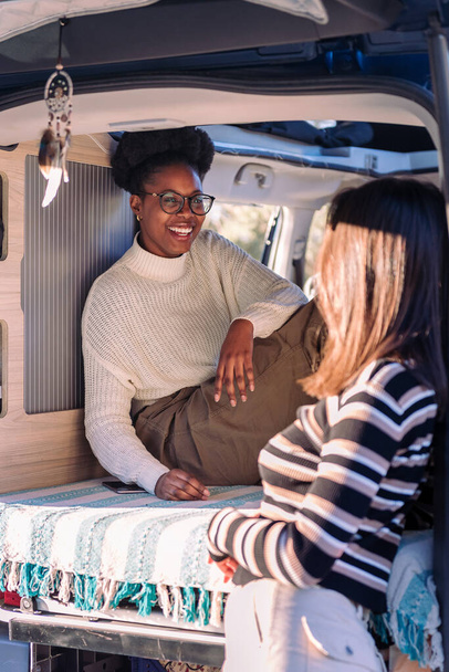african woman laughing in a conversation with friend and enjoying van life, concept of weekend getaway with best friend and relaxation in camper van - Photo, image