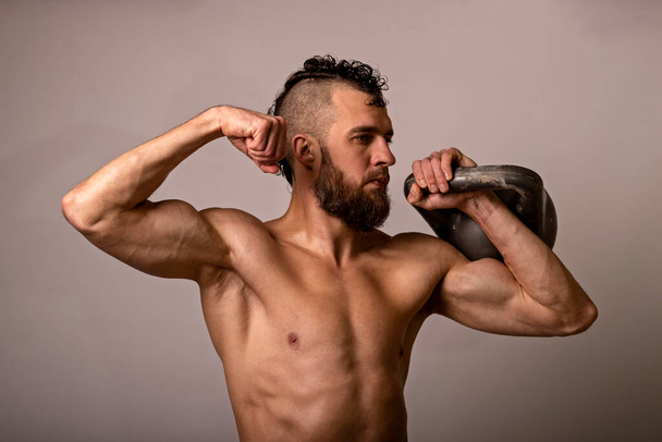 Young muscular man posing with a kettlebell on a light background. Sports lifestyle. - Fotó, kép