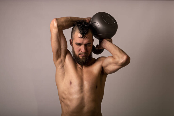 Young muscular man posing with a kettlebell on a light background. Sports lifestyle. - Foto, Bild