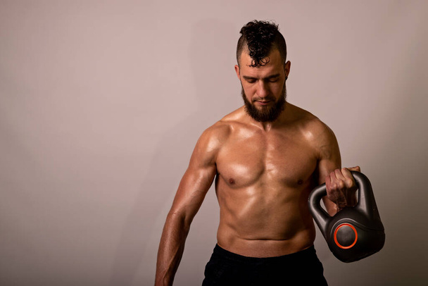 Young muscular man posing with a kettlebell on a light background. Sports lifestyle. - Фото, зображення
