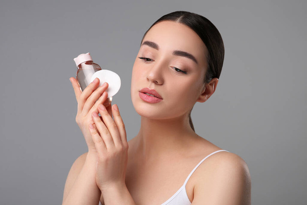 Beautiful woman with makeup remover and cotton pad on gray background - Fotografie, Obrázek
