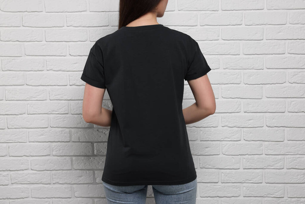 Woman wearing stylish black T-shirt near white brick wall, closeup - Photo, image