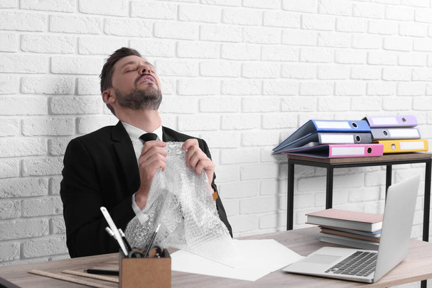 Businessman popping bubble wrap at workplace in office. Stress relief - Foto, immagini