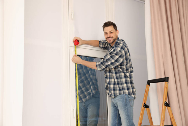 Man measuring window with tape indoors. Roller blinds installation - Foto, afbeelding