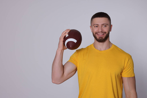 Athletic young man with American football ball on light grey background. Space for text - Fotoğraf, Görsel