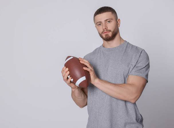 Athletic young man with American football ball on light grey background. Space for text - Foto, immagini