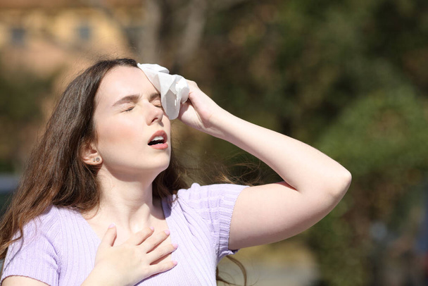 Stressed woman sweating and drying with a tissue in a park in summer - Φωτογραφία, εικόνα