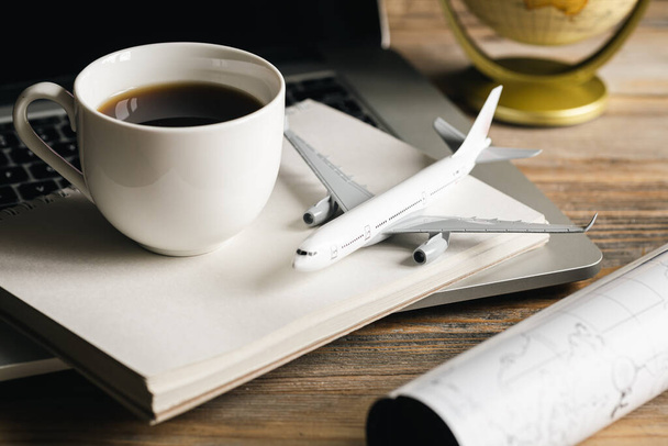 Reissamenstelling met vliegtuigmodel, koffiekop en plattegrond op houten tafel, concept van het vinden van tickets, reisplanning, reisbureau en boeking. - Foto, afbeelding