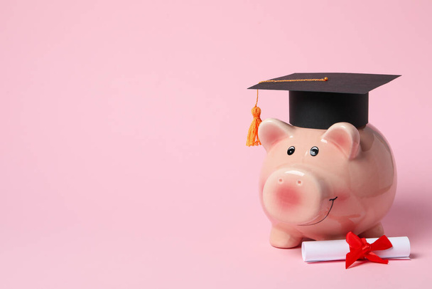 Piggy bank met afstuderen hoed en graad scroll op roze achtergrond - Foto, afbeelding