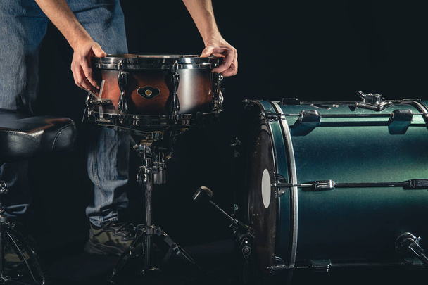 Um baterista masculino e um kit de bateria em um fundo preto, o músico está se preparando para tocar. - Foto, Imagem
