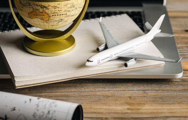 Reisekomposition mit einem Modell eines Flugzeugs und einer Erdkugel auf einem Holztisch, Konzept der Ticketsuche, Reiseplanung, Reisebüro und Buchung. - Foto, Bild