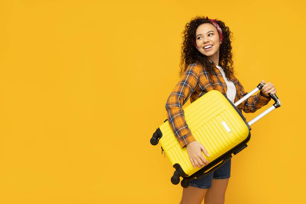 Νεαρή γυναίκα με βαλίτσα σε κίτρινο φόντο - Φωτογραφία, εικόνα