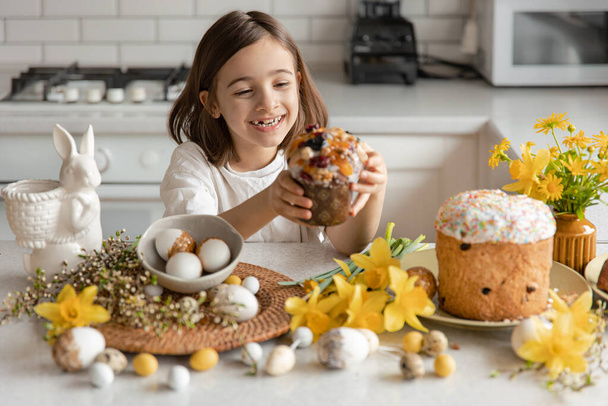 Mutfağın içinde yumurtalı, çiçekli ve bayramlık pastalı bir kek ile komik küçük bir kız. Paskalya için Hazırlık. - Fotoğraf, Görsel