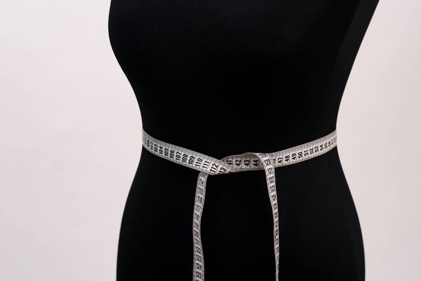 maniquí femenino y una cinta métrica de costura están aislados sobre un fondo blanco. - Foto, Imagen