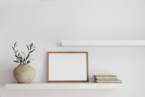 Elegant interior still life. Two floating shelves. Blank wooden picture frame mockup template. Textured vase with olive tree branches and old books. Modern Mediterranean home, white wall background. - Fotoğraf, Görsel