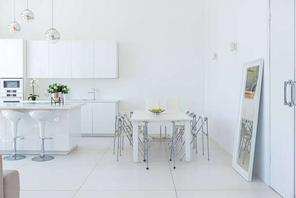 Cozy luxury modern interior design of a studio apartment in extra white colors with fashionable expensive furniture in a minimalist style. white tiled floor, kitchen, relaxation area and workplace - Foto, afbeelding