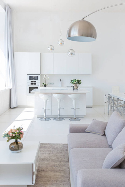 Cozy luxury modern interior design of a studio apartment in extra white colors with fashionable expensive furniture in a minimalist style. white tiled floor, kitchen, relaxation area and workplace - Foto, Imagen