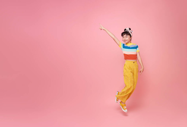 Menina asiática pulando para cima e apontando o dedo isolado em rosa cópia espaço estúdio fundo. - Foto, Imagem