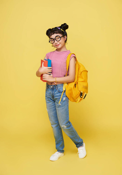 Full body smiling happy cheerful teen Asian student girl hold backpack book isolated on yellow background. Education in school concept - Фото, изображение