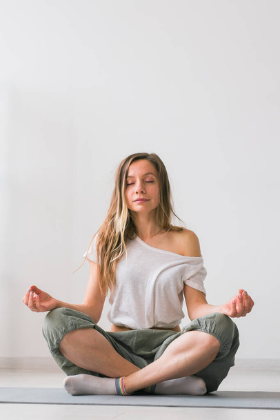 Joven mujer hermosa sana practicando yoga en casa sentada en postura de loto sobre esterilla de yoga meditando sonriendo relajada con los ojos cerrados - Meditación Mindfulness - Foto, Imagen