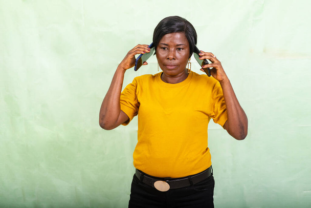 kaunis nainen keltaisessa t-paidassa seisoo vihreällä taustalla puhumassa matkapuhelimessa samanaikaisesti. - Valokuva, kuva